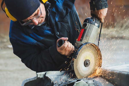 Worker saws metal with an old angle grinder. selective focus. outdoors. flying sparks. industrial conceptの写真素材