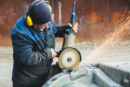 Worker saws metal with an old angle grinder. selective focus. outdoors. flying sparks. industrial conceptの写真素材