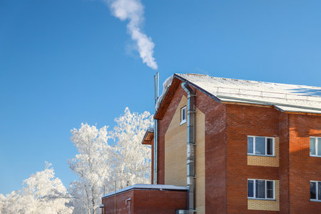 Smoke from the chimney of a private house with its own boiler room. Cold frost winter. Season specificの写真素材
