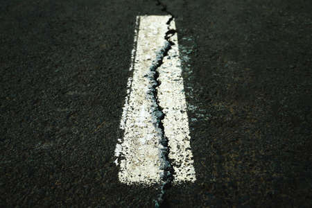 Worn white road line on cracked asphalt close-upの写真素材