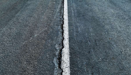 Worn white road line on cracked asphalt close-upの写真素材