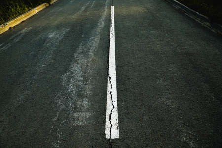 Worn white road line on cracked asphalt close-upの写真素材