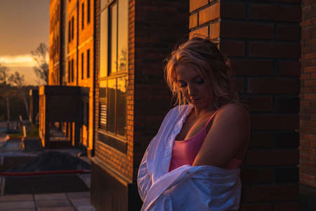 The dark portrait of a young woman with makeup at sunset against the background of a brick wallの写真素材