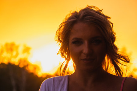 Portrait of a girl against the background of a fiery orange sunsetの写真素材