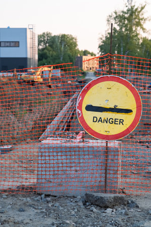 Shabby danger sign on the background of construction site and excavatorの写真素材
