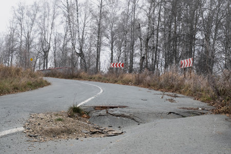 Pothole damage on a rural road surrounded by trees in autumn highlights urgent need for repairsの写真素材