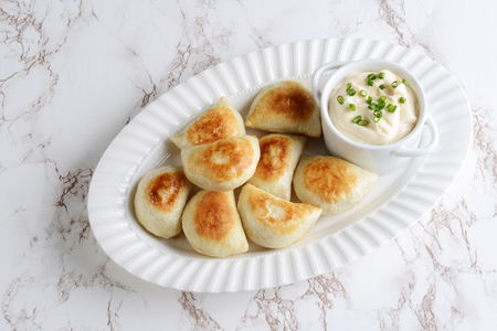 top view pierogies on a white platter with sour cream and spring onionsの写真素材