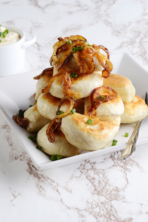 closeup pile of pierogies with sour cream caramelized onions and a forkの写真素材