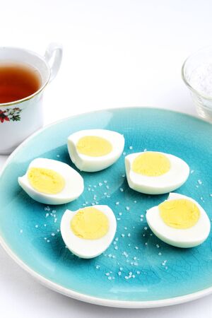 sliced boiled eggs on a blue plate with saltの写真素材
