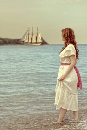 vintage style woman walking in ocean with tall shipの写真素材