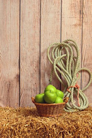 green apples in basket with rope on straw baleの写真素材