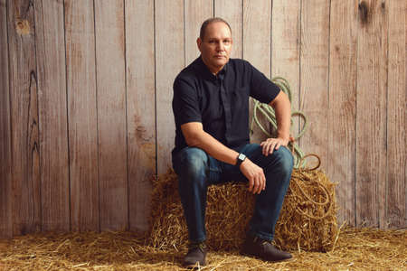 portrait of man resting on hay bale in barnの写真素材