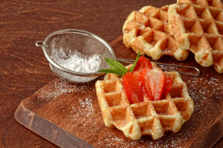 hot belgian waffles with strawberries on cutting boardの写真素材