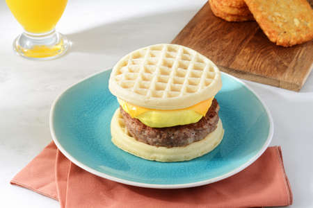 breakfast sausage egg cheese waffles sandwich with hash brownsの写真素材