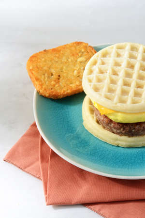 closeup of scrambled egg sausage waffle sandwich with hash brownの写真素材