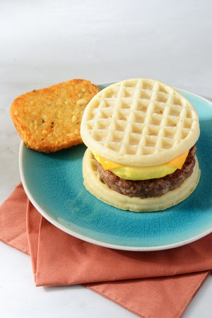 scrambled egg sausage waffle sandwich with hash brownの写真素材