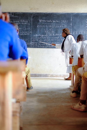 Kibuye/Rwanda - 08/26/2016: Teacher and pupils at mathematics lesson in a classroom in a school in Africa. A blackboard and cross can be seen in the background.のeditorial素材