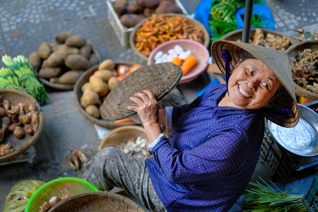 Hoi An / Vietnam, 12/11/2017: Local vietnamese woman smiling and selling vegetables on a traditional street market in Hoi An, Vietnam.のeditorial素材