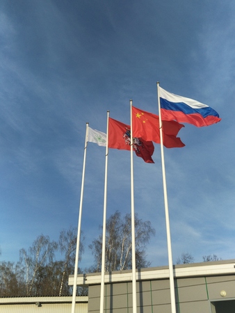 four flags flutter in the wind against the bright blue sky, Chinese red with five stars, Russian tricolour, the flag of Moscow and Sokolniki Park of culture and Rest. video. friendship of peoples.の写真素材