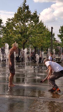 Moscow, RF Sept, 01 2019: Street photo. A couple of people having fun in the city fountain. A woman frolics in the jets of water, a man shoots a video on his smartphone. Warm sunny day. September day off.のeditorial素材