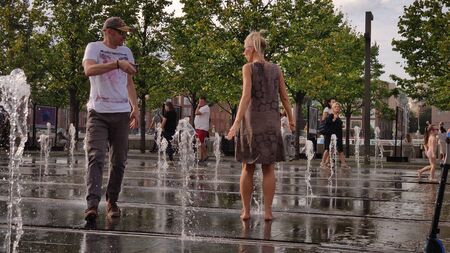 Moscow, RF Sept, 01 2019: Street photo. A couple of people having fun in the city fountain. A woman frolics in the jets of water, a man shoots a video on his smartphone. Warm sunny day. September day off.のeditorial素材