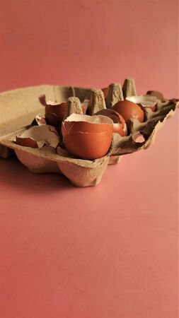 Eggshell halves in recycled cardboard packaging on a pink background. Broken eggs in a craft box, coral-colored surface. Empty shells in cardboard boxes. Processing of food waste, ecology, reuse of natural resources, preservation of the environment. Side view.の写真素材