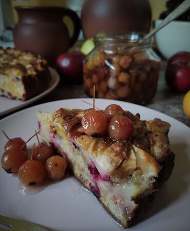 Blurred background. A slice of Apple pie and a jam of Paradise apples with a stalk on a pink round plate. In the background ceramic utensils, mug and pot, fruits. Still life in pastel natural colors, rustic.の写真素材