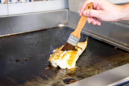 The process of cooking white fish in a restaurant. Using a wooden brush, a professional chef smears...