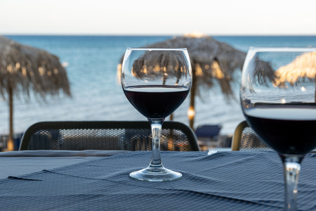 two glasses of red wine on a table at sunset on beach in summerの写真素材