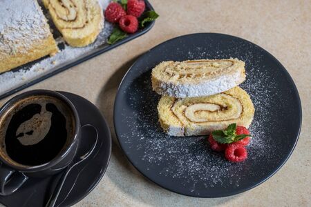 Swiss Roll with jam, decorated with raspberries and mint on a plate and black coffee. Sweets....