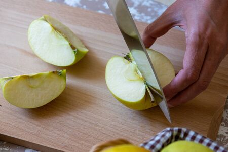 Woman cuts by knife an apple to slices on a cutting board on a table in the kitchen. Chauntecleer apples. Cooking food.の写真素材