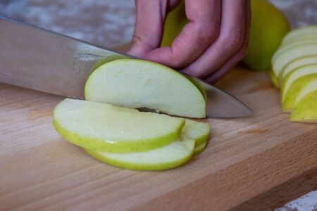 Woman cuts by knife an apple to slices on a cutting board on a table in the kitchen. Chauntecleer apples. Cooking food.の写真素材