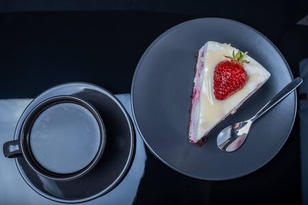 fresh cream fruit cake and a cup of black coffee on a black glass tableの写真素材