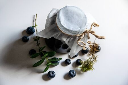 A can of blueberry jam and blueberries on a white table. huckleberry jam.の写真素材