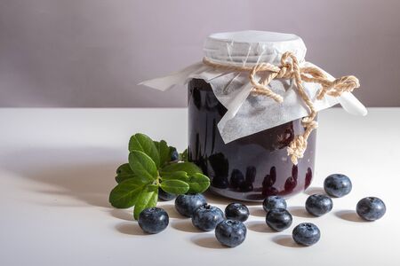 A can of blueberry jam and blueberries on a white table. huckleberry jam.の写真素材