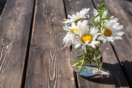 bouquet of white daisies in a glass vase on a wooden table.の写真素材