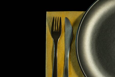 metal fork, knife on yellow napkin and plate on a black background. top view on stainless knife and fork with copy space.の写真素材