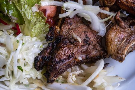 Lamb breast slices garnished with fresh vegetables and potatoes. Plate with meat and onion.の写真素材