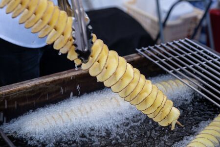 Potatoes sliced â€‹â€‹in a thin spiral on a skewer will be boiled in boiling oil.