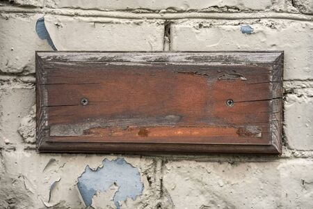 Old cracked wooden plate on a brick wall. white brick wall. Concept of nameplate.