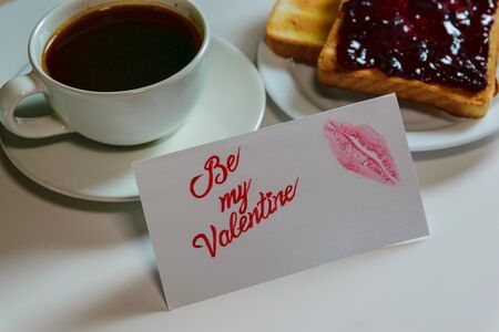 Roasted toast with blueberry jam and black coffe on the white table. Be My Valentine white message card with lips imprint.の写真素材