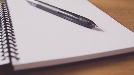 Closeup of a black pen on a notebook. Notepad open on a blank page on the table.の写真素材