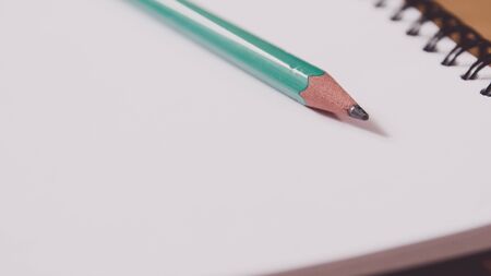 Closeup of a green pencil on a notebook. Notepad open on a blank page on the table.の写真素材