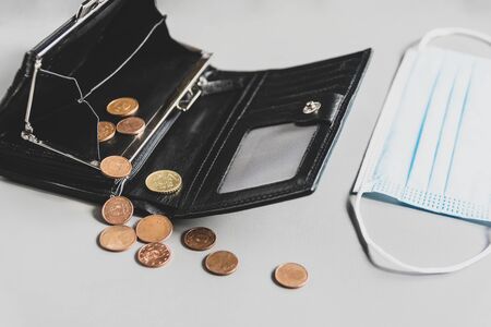 Opened empty black wallet, couple of coins  and medical mask on a gray table. money is over due to...