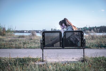 Beautiful sad woman sitting on the wooden bench on the riverside.の写真素材