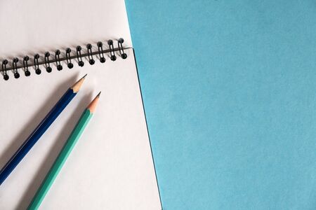 pencils and spiral notebook on a pastel light background. Notebook with blank clear page on the...