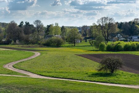 Empty winding rural road along fields and a small village in sunny day.の写真素材