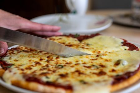 Woman cuts by slices homemade vegetarian pizza with tomatoes and mozzarella cheese.の写真素材