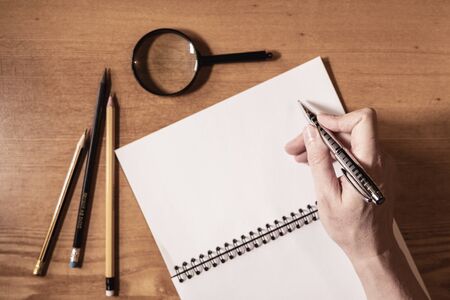 women hand holding a pen to write on her notebook on a wooden table.