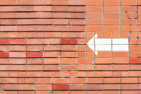 Red brick wall with a painted white arrow pointing in the direction.
